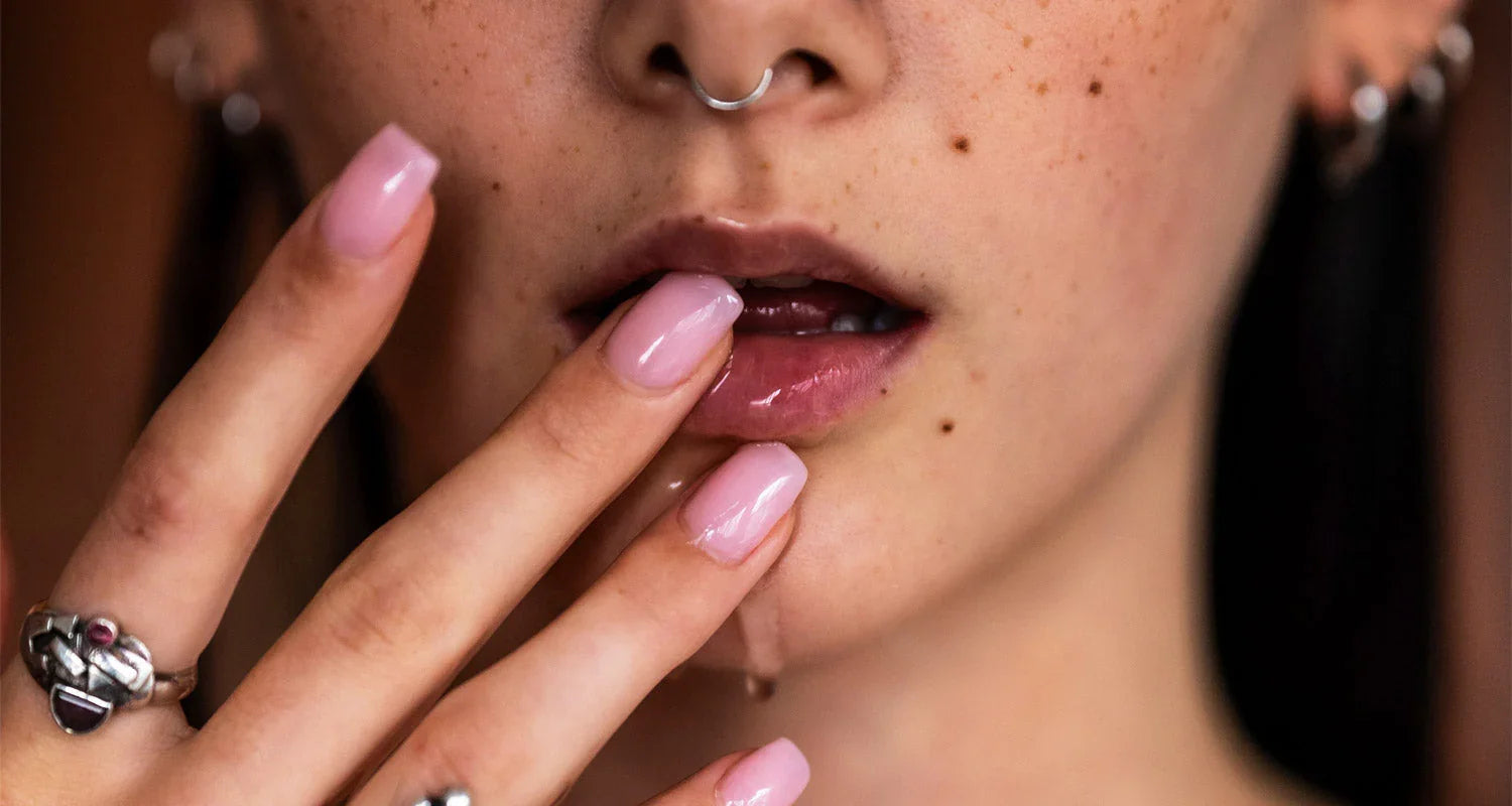 Close-up of a person with pink nail polish and a nose ring, with a blurred background.