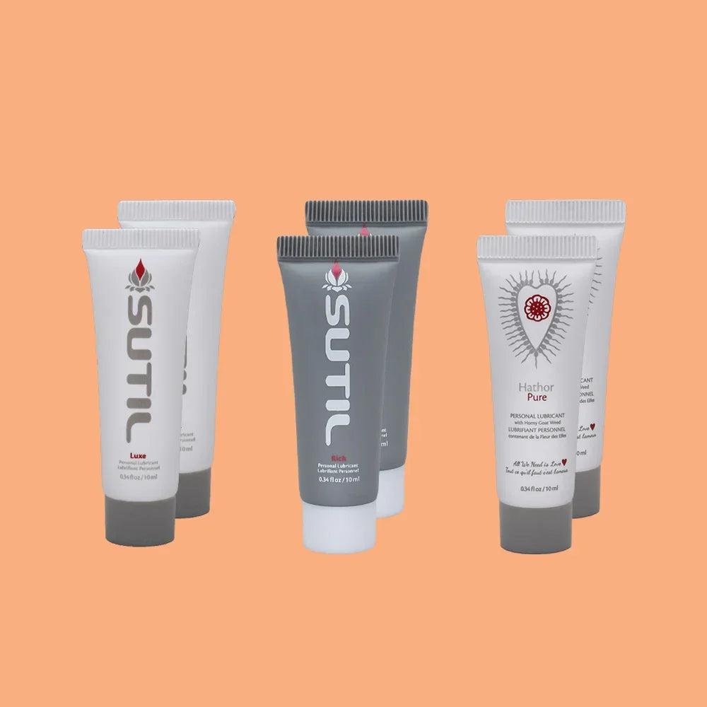Three portable tubes of Sutil intimate lubricants, Rich, Luxe, and Hathor Pure, against an orange background.